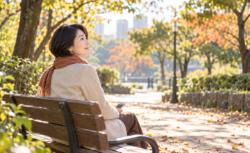 木漏れ日の公園のベンチで、スマートフォンを手に穏やかに過ごす女性